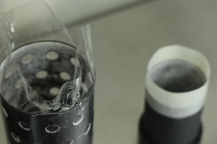 Dois cilindros de microfusão, um perfurado com colar de película e outro com colar de papel, prontos para o revestimento